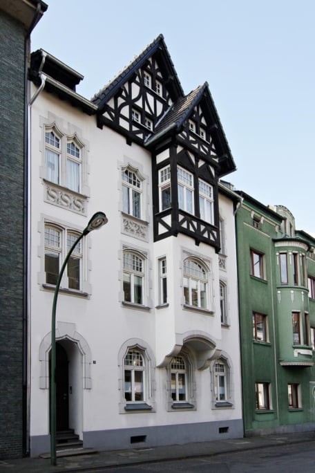 Das Prinzip Dachwohnung. Dachgeschossumbau im Denkmal., Düsseldorf-Oberrath — Straßenfassade von 1905 mit weiß verputztem Erdgeschoss und dunklem Fachwerkgiebel im Dach