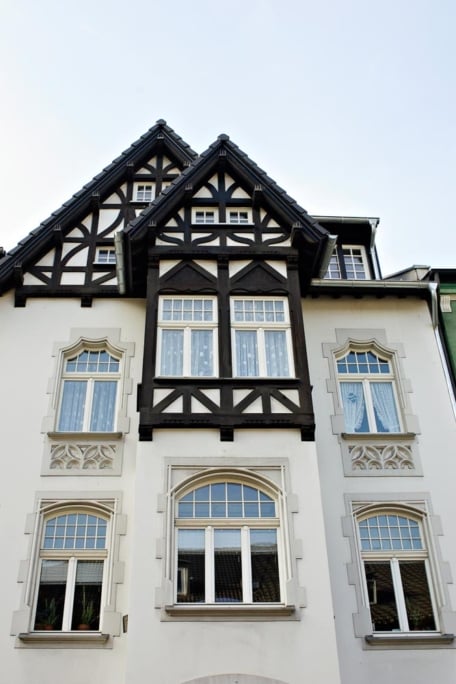 Das Prinzip Dachwohnung. Dachgeschossumbau im Denkmal., Düsseldorf-Oberrath — Nahaufnahme des Zwerchgiebels: dunkles Fachwerk vor hellem Putz, darunter Sprossenfenster