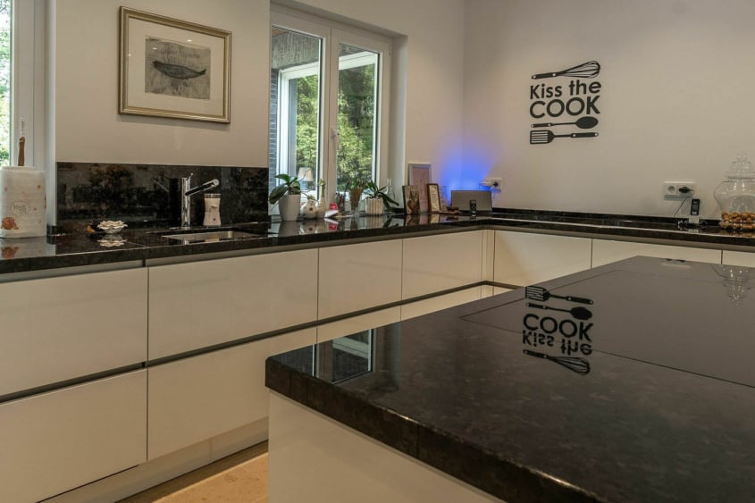 Entwurf im Waldhaus, Mönchengladbach-Hardt — Kücheninsel mit schwarzer Granitplatte und mattierten Glasfronten vor Fenstern zum Wald
