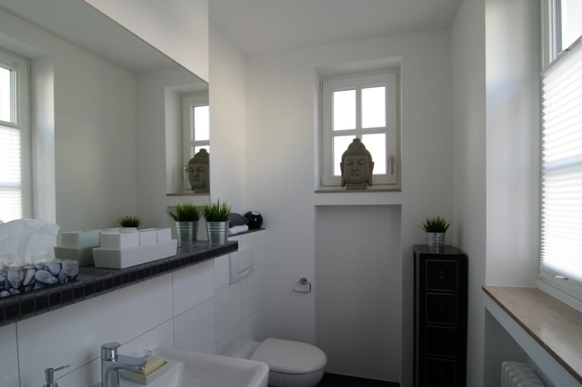Sanierung historischer Bausubstanz, Monheim am Rhein — Helles Bad im ehemaligen Waschhaus mit weißem Waschtisch, Wandspiegel und Buddha-Figur — Innenarchitektur von Bernd Schüller