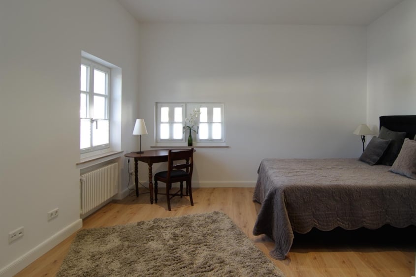 Sanierung historischer Bausubstanz, Monheim am Rhein — Schlafzimmer mit Holzdielen, kleinem Schreibtisch am Fenster und bezogenem Bett