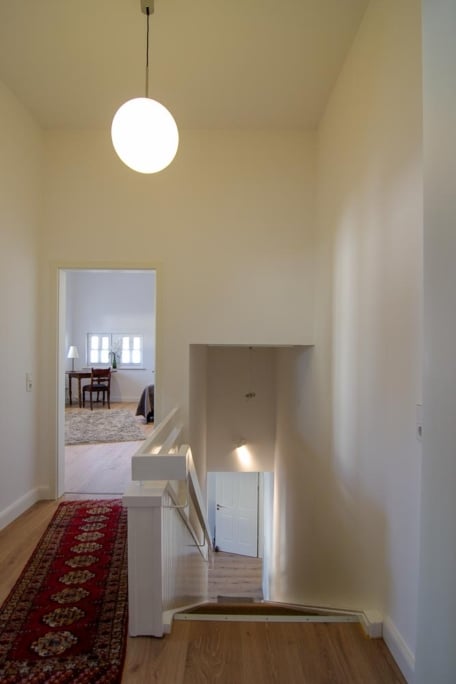 Sanierung historischer Bausubstanz, Monheim am Rhein — Foyer mit runder Hängeleuchte, rotem Läufer und Treppenabgang im Hintergrund