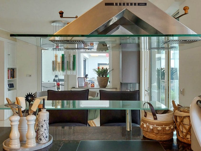 Transformation eines Einfamilienhauses, Langenfeld (Rheinland) — Offene Küche mit Glasablage vor spiegelnder Pyramiden-Dunstabzugshaube, dahinter der Essbereich