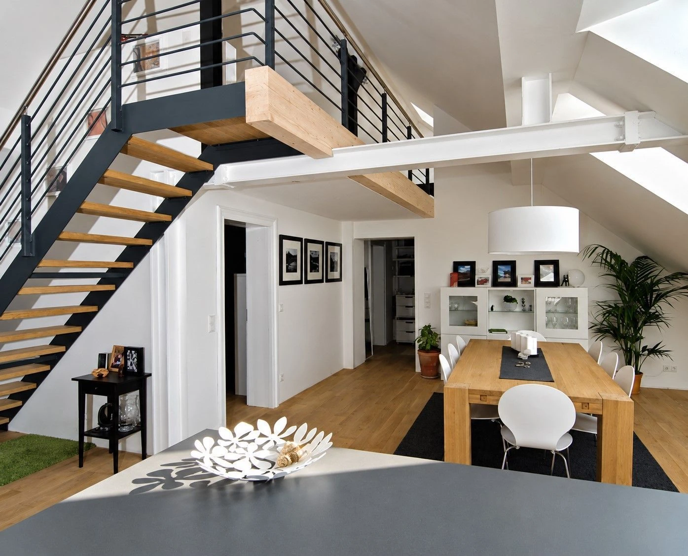 Das Prinzip Dachwohnung. Dachgeschossumbau im Denkmal., Düsseldorf-Oberrath — Essbereich unter offener Galerie mit Stahl-Holz-Treppe und weißem Träger in Düsseldorf-Oberrath — Denkmalumbau von Bernd Schüller