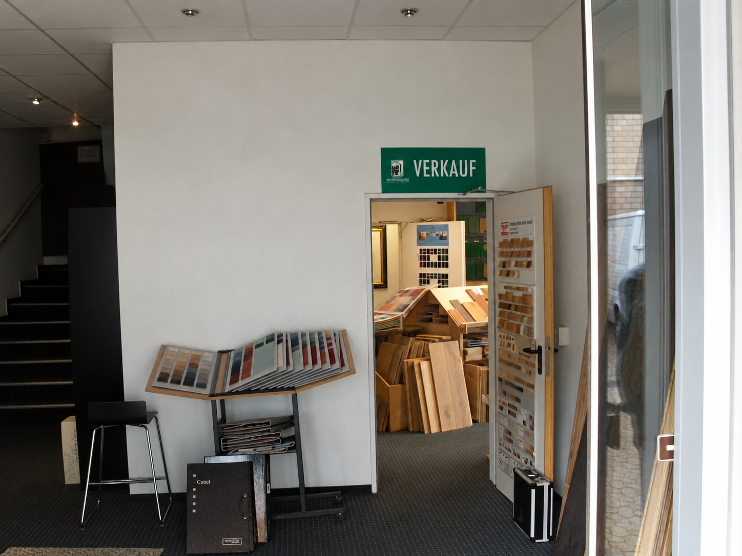 Eingang des Großhandels mit Materialständer, Verkaufsschild und dunkler Treppe